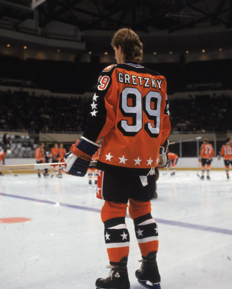 Gretzky from behind on the ice, wearing an orange and black Chicago Blackhawks jersey with 'GRETZKY' and the number '99' on the back.