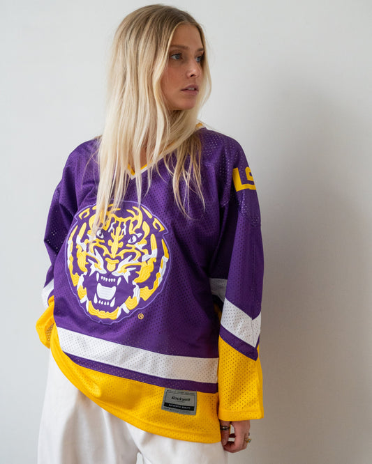 A blonde woman wears a retro LSU Tigers hockey jersey with a white wall and shadows behind her