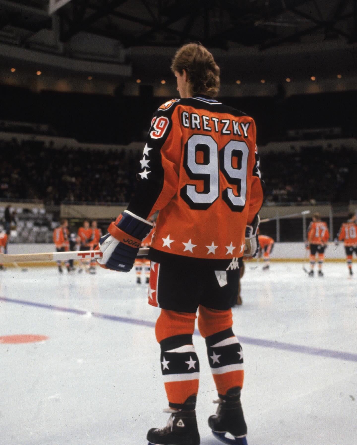Gretzky from behind on the ice, wearing an orange and black Chicago Blackhawks jersey with 'GRETZKY' and the number '99' on the back.