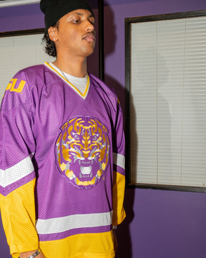 Person wearing a purple and yellow sports jersey with a tiger logo against a purple wall.