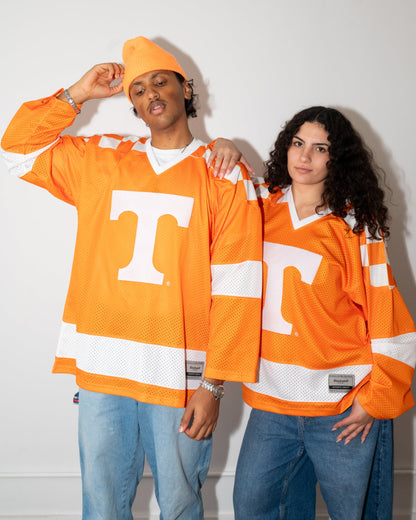 Two models wearing matching bright orange Tennessee Volunteers hockey jerseys with a large white 'T' logo, standing against a plain light gray wall.